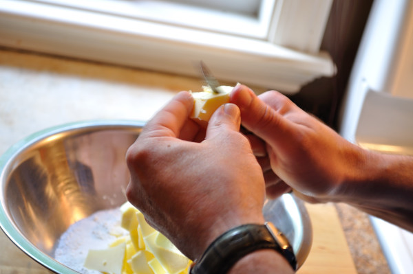 Two hands cutting butter into a bowl of dry ingredients.